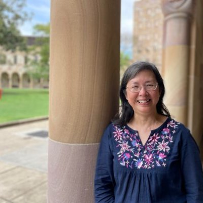 Dr Poh Hillock standing outside a sandstone building with trees behind her.